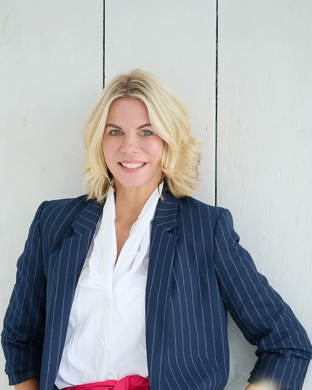 Modern corporate headshot of a woman in a dark navy pinstripe blazer against a light wood wall.