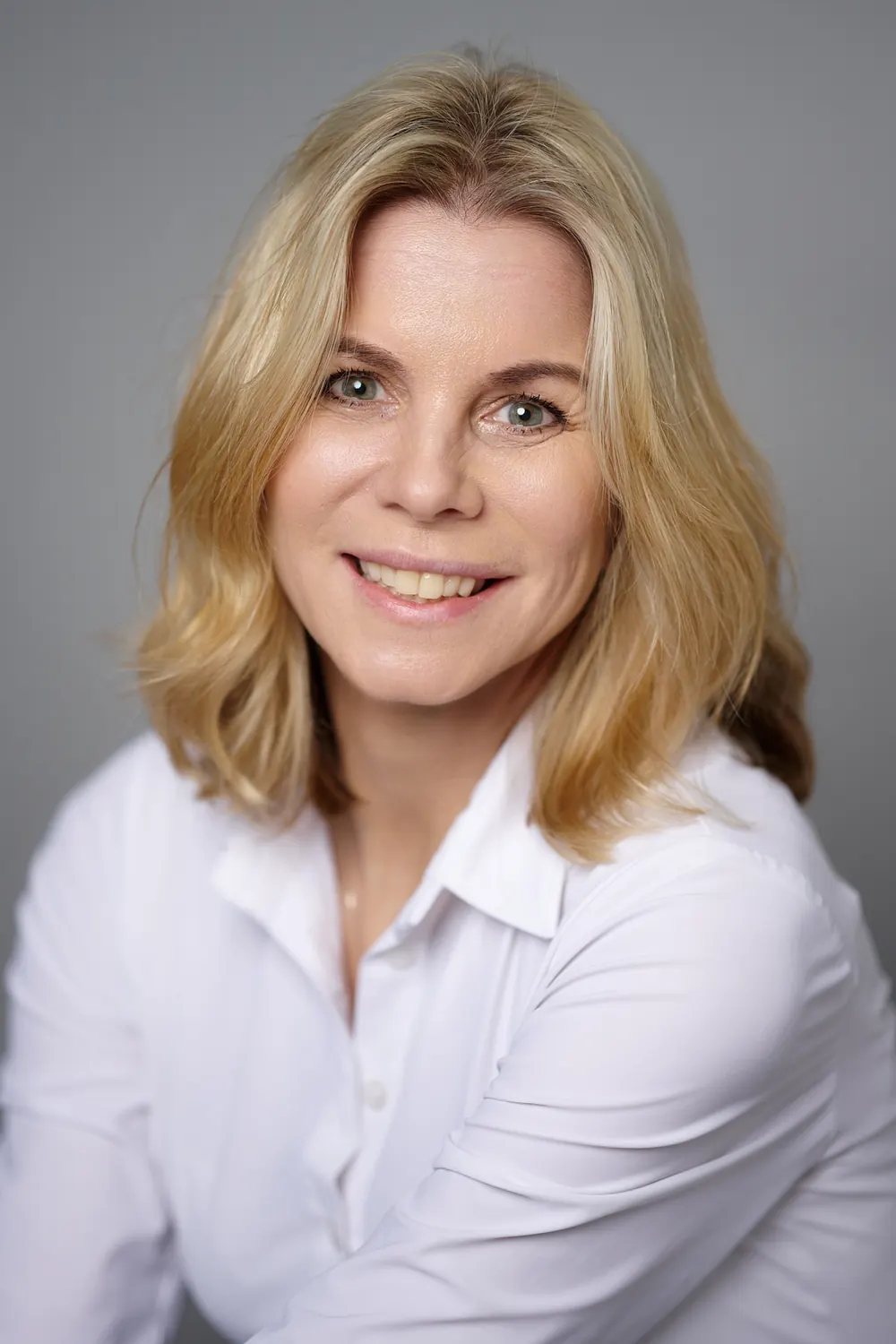 Natural LinkedIn portrait of a woman in a white blouse against a grey background.